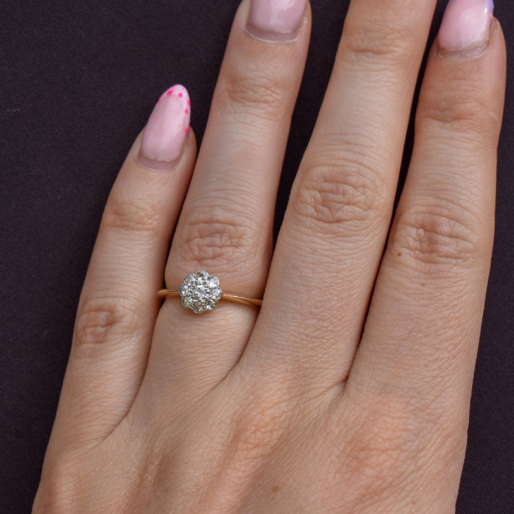 An antique diamond daisy cluster ring set in platinum with an 18ct yellow gold band resting inside an open red heart-shaped velvet box. View III
