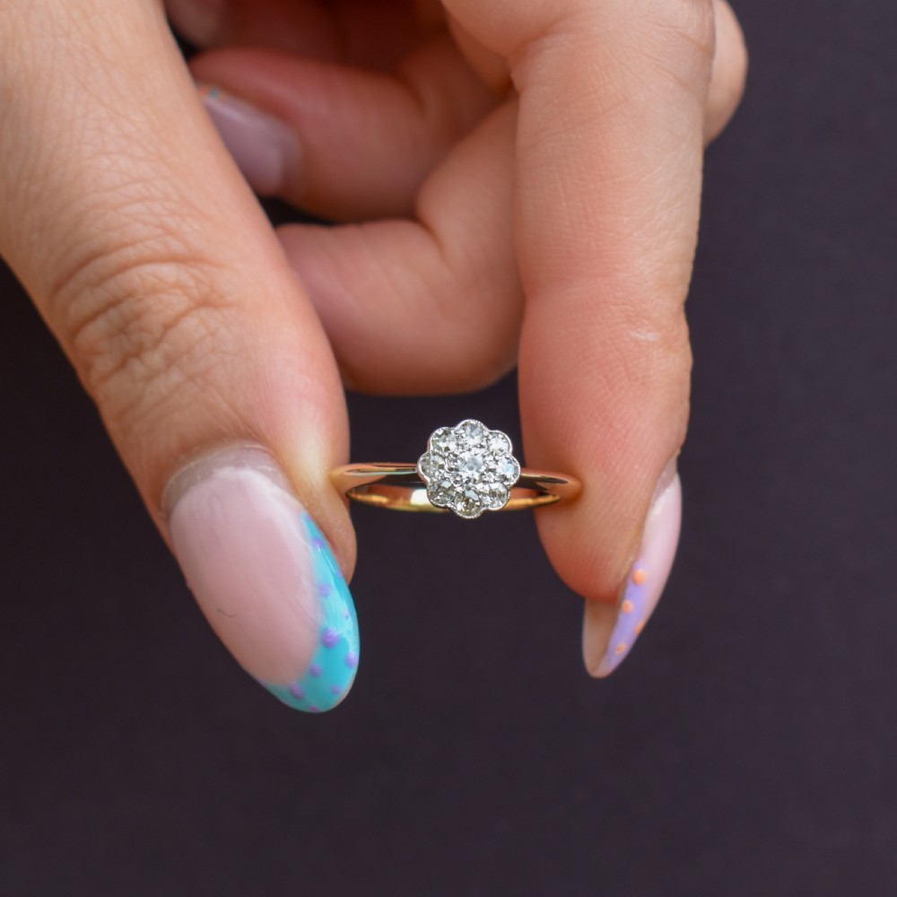 An antique diamond daisy cluster ring set in platinum with an 18ct yellow gold band resting inside an open red heart-shaped velvet box. View IV
