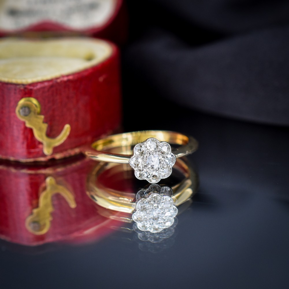 An antique diamond daisy cluster ring set in platinum with an 18ct yellow gold band resting inside an open red heart-shaped velvet box. View VII