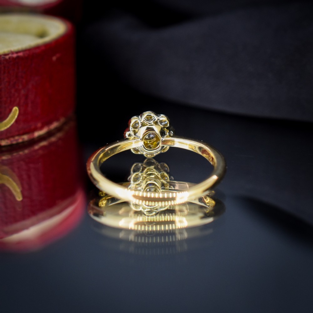 An antique diamond daisy cluster ring set in platinum with an 18ct yellow gold band resting inside an open red heart-shaped velvet box. View IX