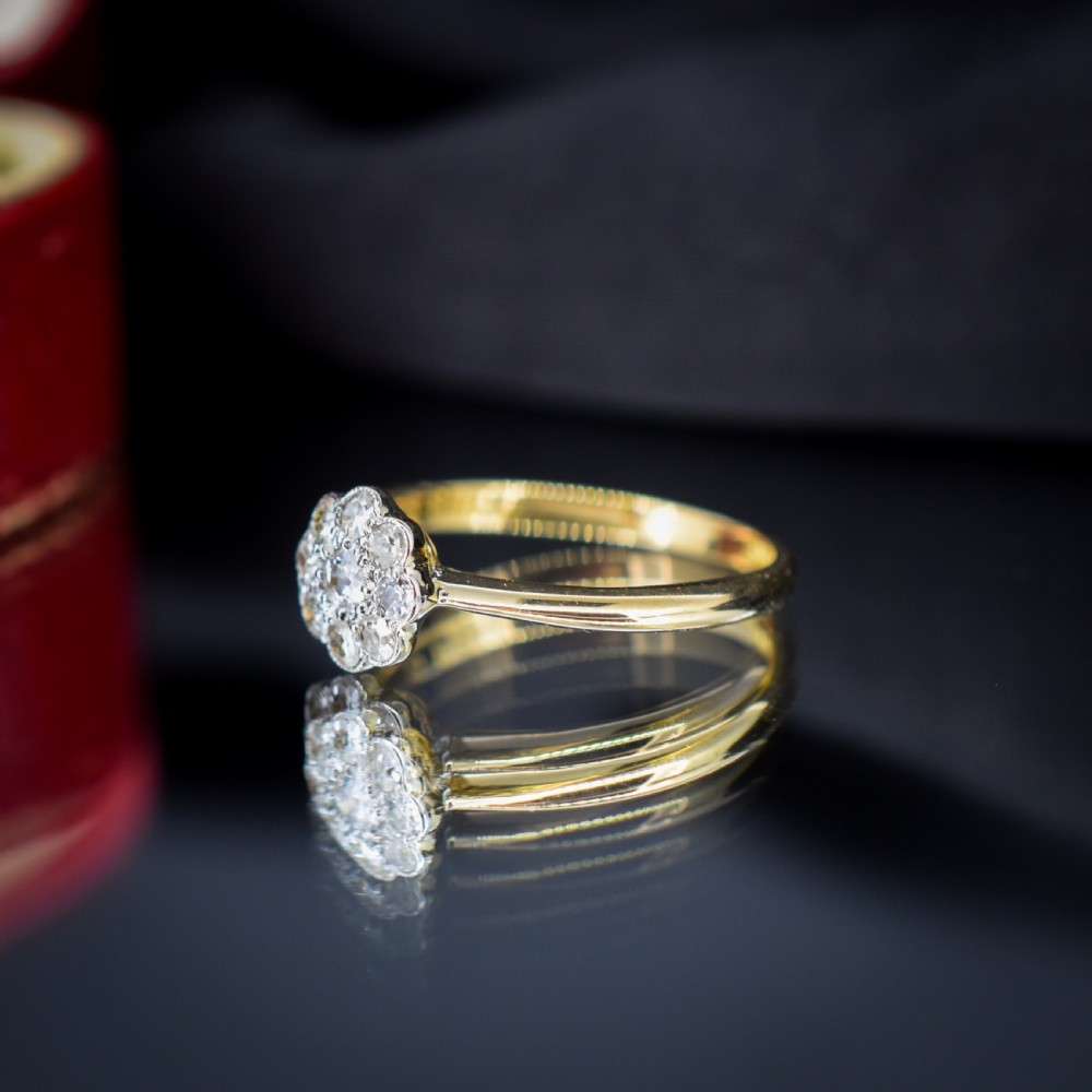 An antique diamond daisy cluster ring set in platinum with an 18ct yellow gold band resting inside an open red heart-shaped velvet box. View X