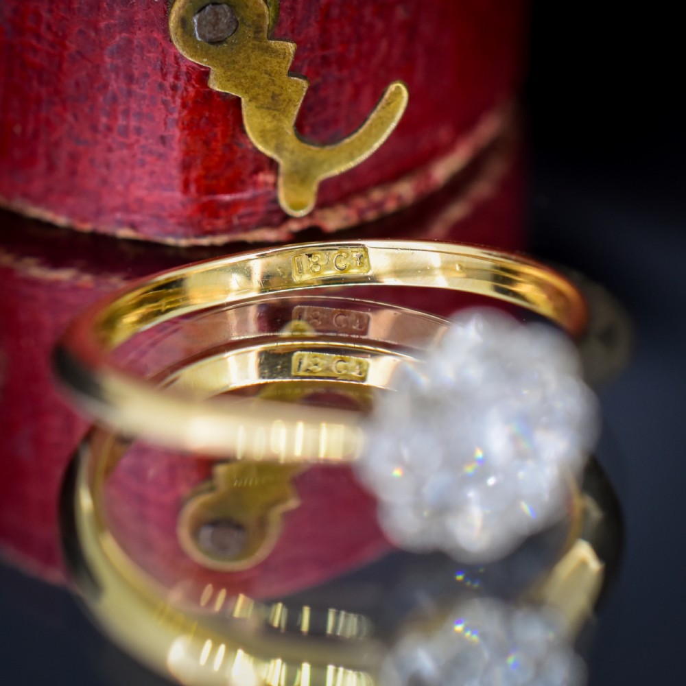 An antique diamond daisy cluster ring set in platinum with an 18ct yellow gold band resting inside an open red heart-shaped velvet box. View XI