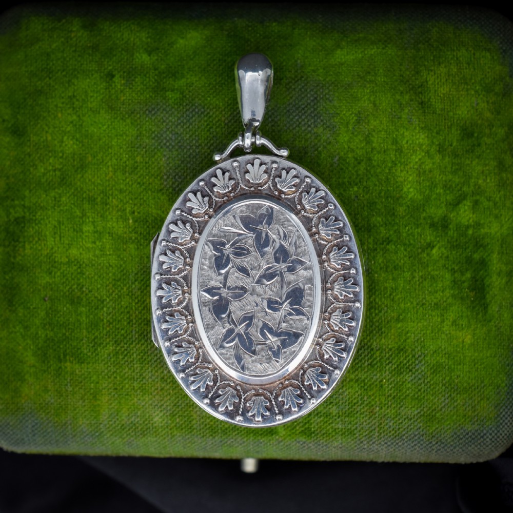 A Victorian oval sterling silver photo locket featuring a central hand-engraved ivy leaf motif framed by an anthemion border.
