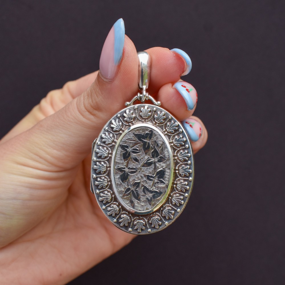 A Victorian oval sterling silver photo locket featuring a central hand-engraved ivy leaf motif framed by an anthemion border. View X