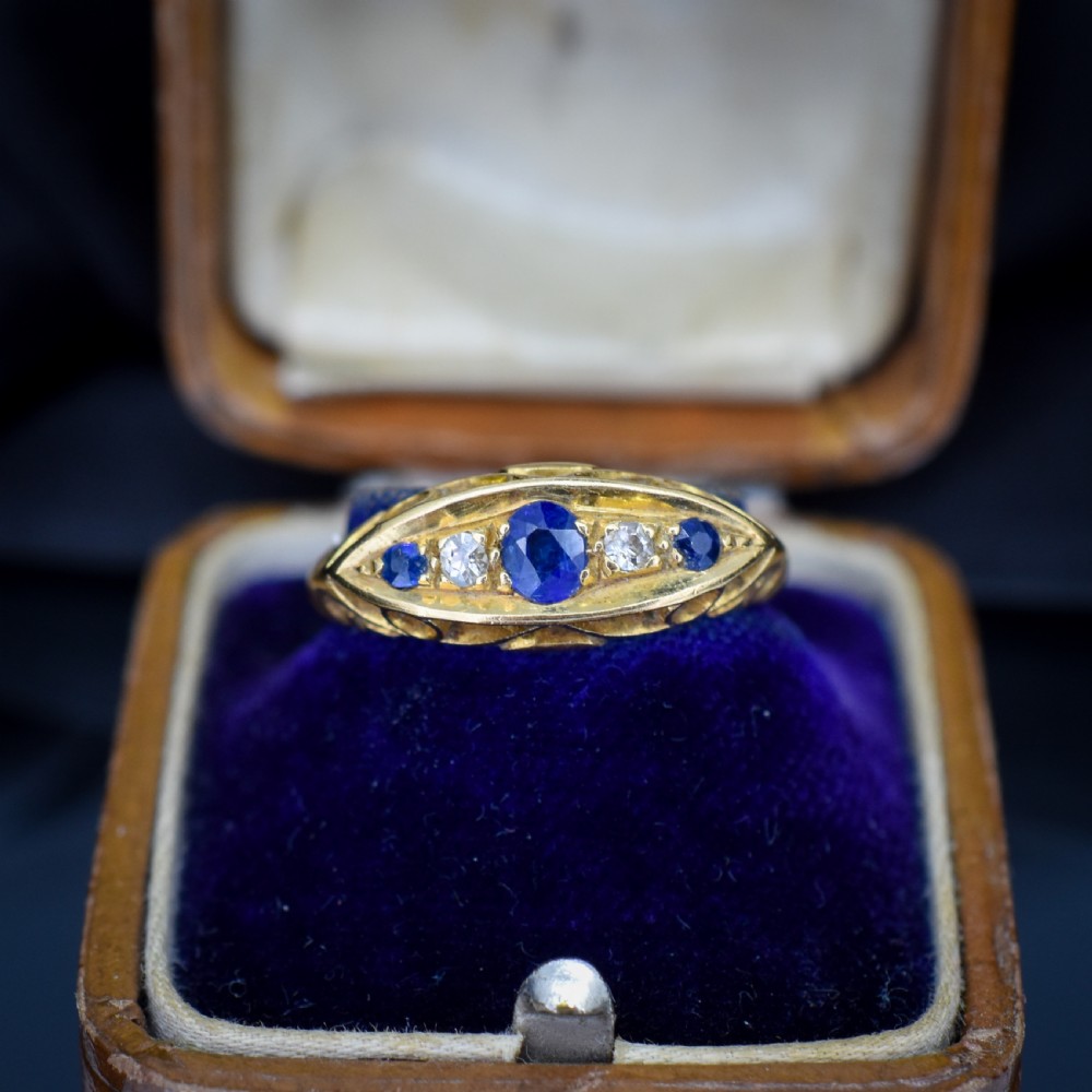 An Edwardian 18ct yellow gold boat ring set with three blue sapphires and two diamonds in an elongated marquise-shaped mount.