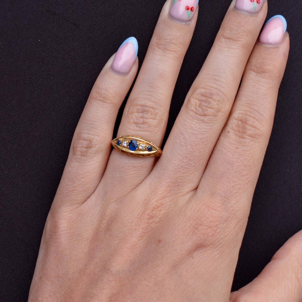 An Edwardian 18ct yellow gold boat ring set with three blue sapphires and two diamonds in an elongated marquise-shaped mount. View VI