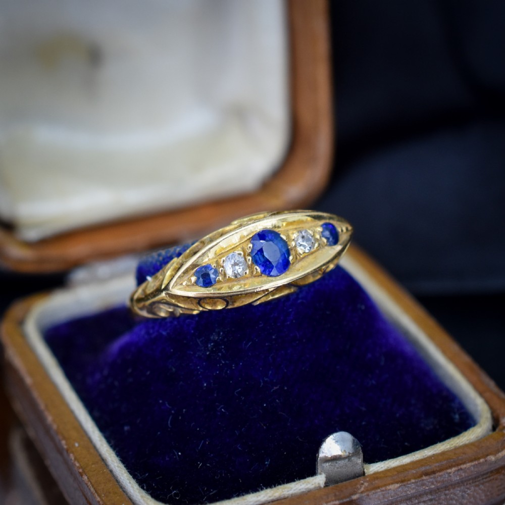 An Edwardian 18ct yellow gold boat ring set with three blue sapphires and two diamonds in an elongated marquise-shaped mount. View VII