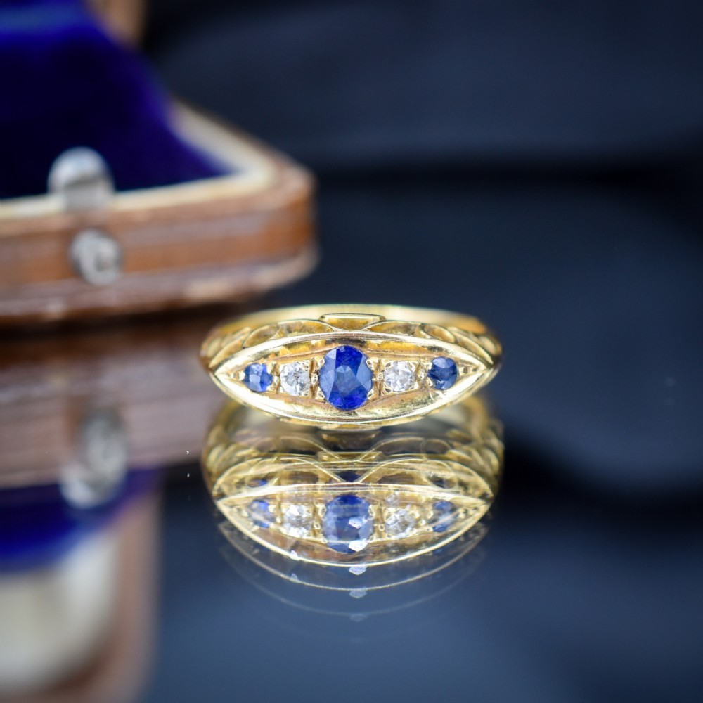 An Edwardian 18ct yellow gold boat ring set with three blue sapphires and two diamonds in an elongated marquise-shaped mount. View IX