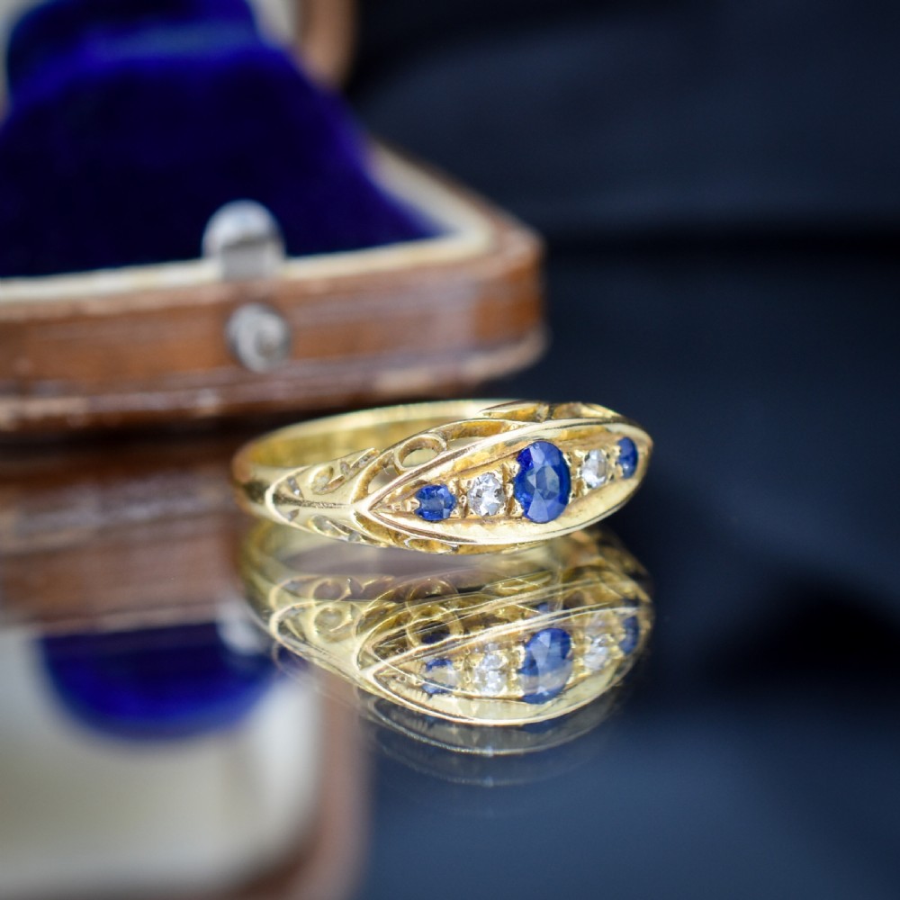 An Edwardian 18ct yellow gold boat ring set with three blue sapphires and two diamonds in an elongated marquise-shaped mount. View X