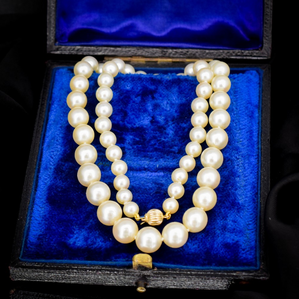 A graduated strand of cream pearls featuring a yellow gold fluted clasp.