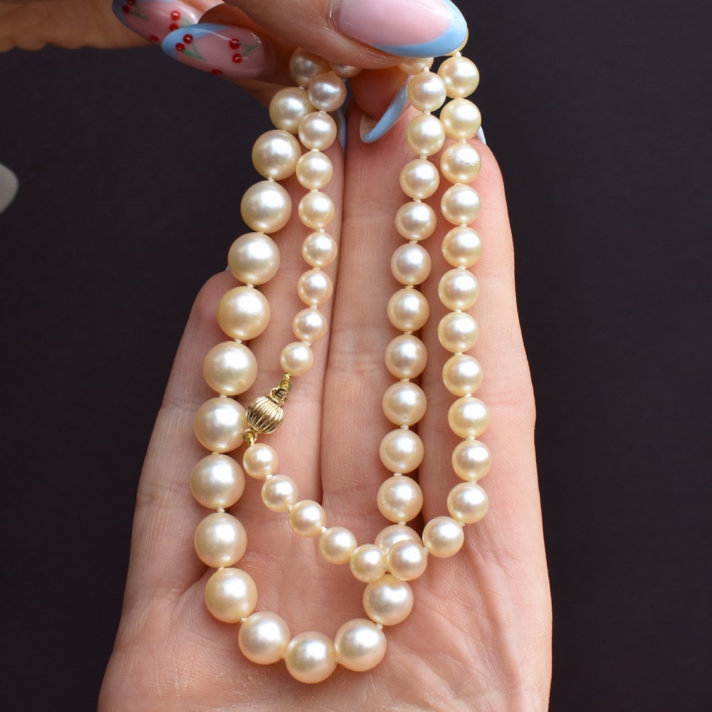 A graduated strand of cream pearls featuring a yellow gold fluted clasp. View IX