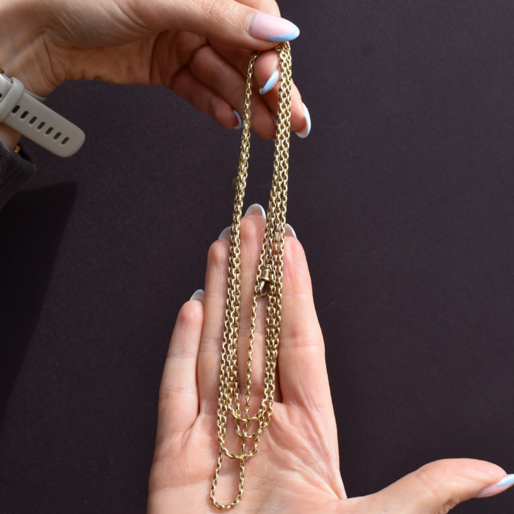 A long 9ct yellow gold faceted link guard chain wrapped in loops beside a swivel dog clip clasp. View VIII