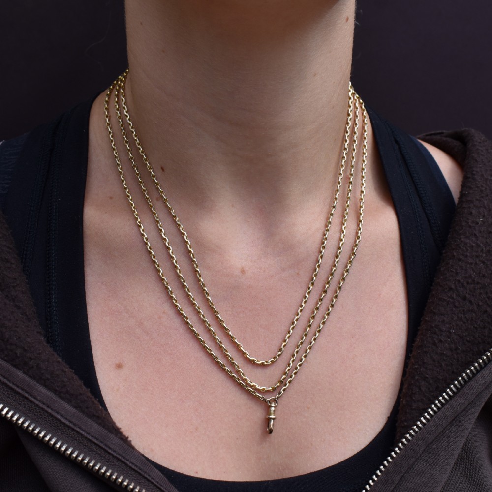 A long 9ct yellow gold faceted link guard chain wrapped in loops beside a swivel dog clip clasp. View X