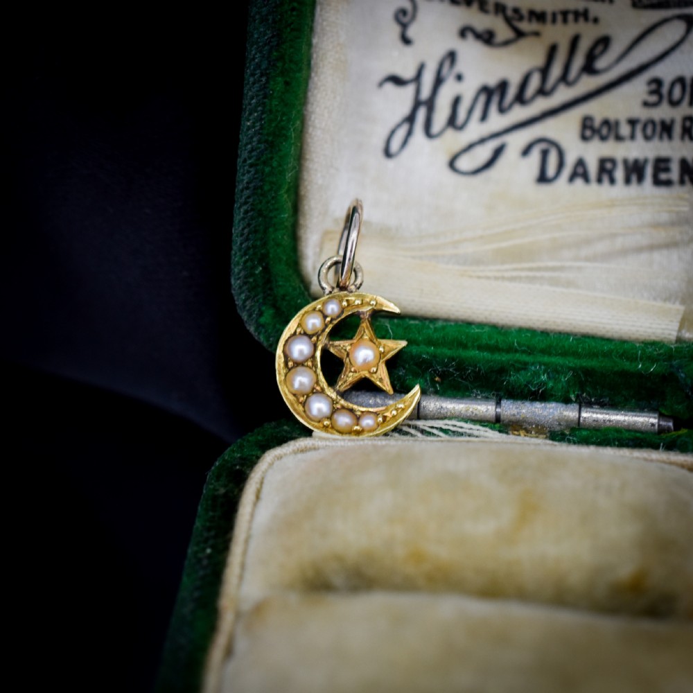 An 18ct gold crescent moon pendant set with seed pearls enclosing a star motif.