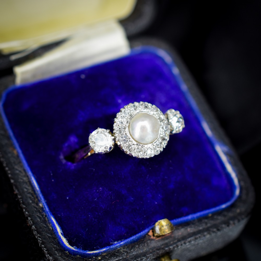 An Edwardian 18ct yellow gold ring featuring a central round pearl framed by a halo of small diamonds and two shoulder-set diamonds. View III
