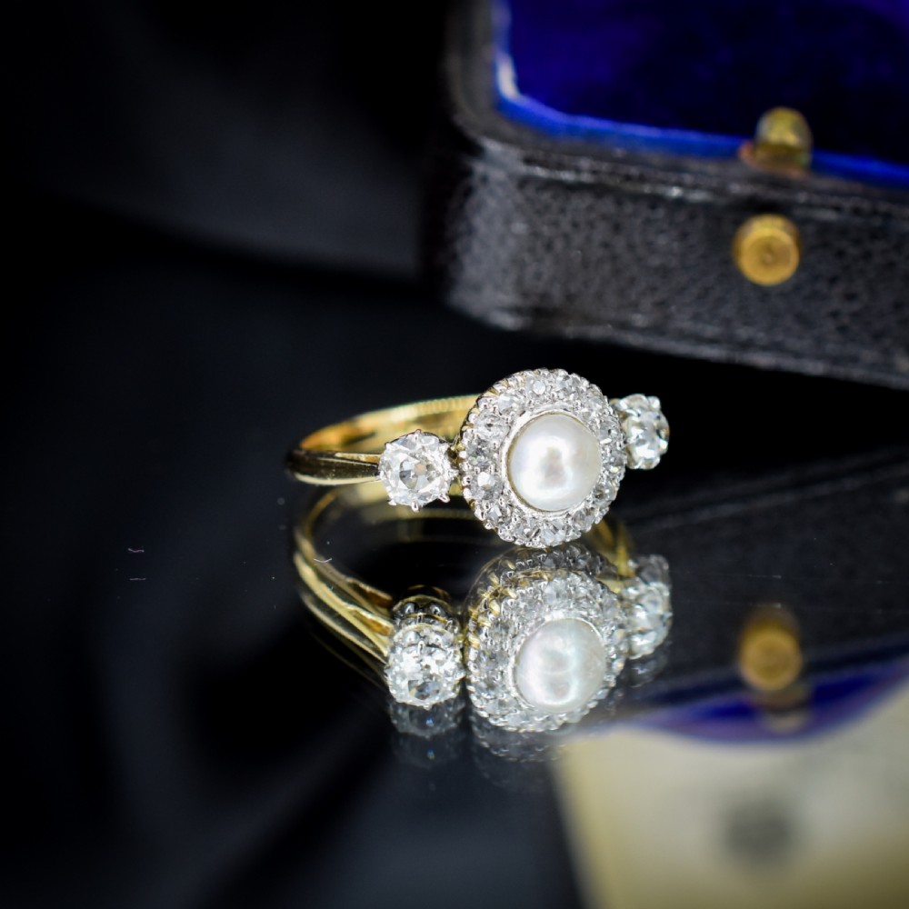 An Edwardian 18ct yellow gold ring featuring a central round pearl framed by a halo of small diamonds and two shoulder-set diamonds. View V