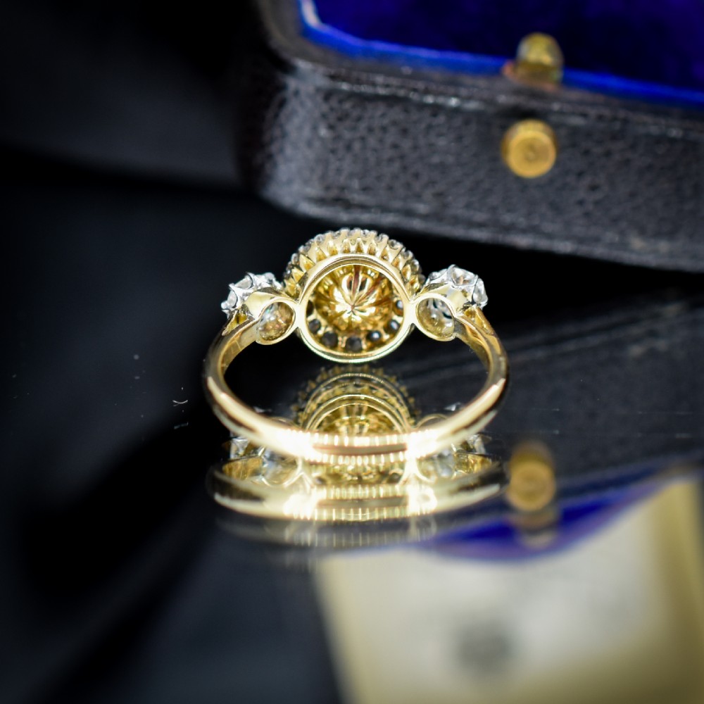 An Edwardian 18ct yellow gold ring featuring a central round pearl framed by a halo of small diamonds and two shoulder-set diamonds. View VI