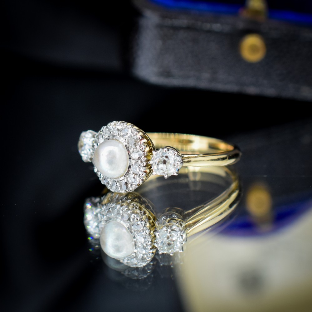 An Edwardian 18ct yellow gold ring featuring a central round pearl framed by a halo of small diamonds and two shoulder-set diamonds. View VII