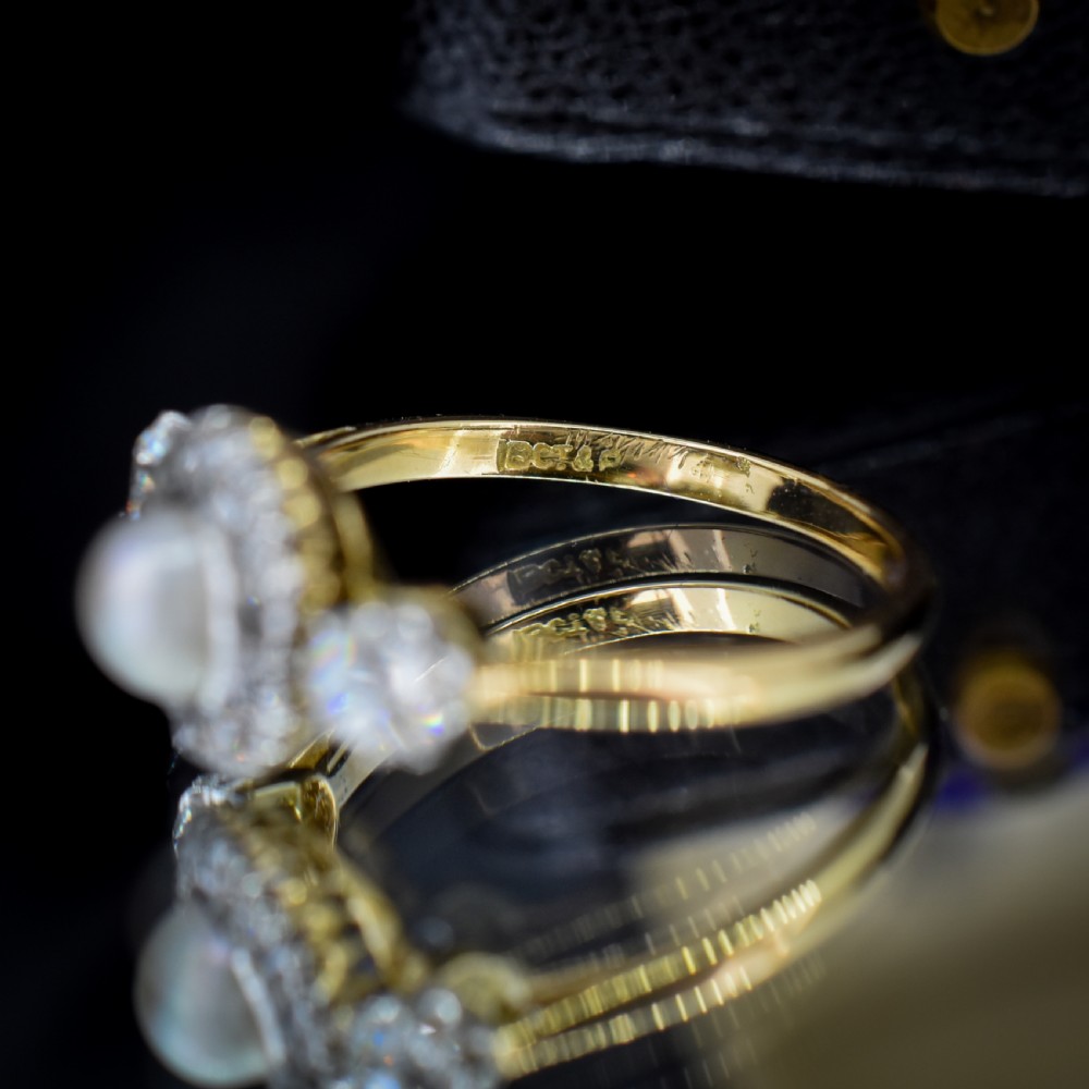 An Edwardian 18ct yellow gold ring featuring a central round pearl framed by a halo of small diamonds and two shoulder-set diamonds. View VIII