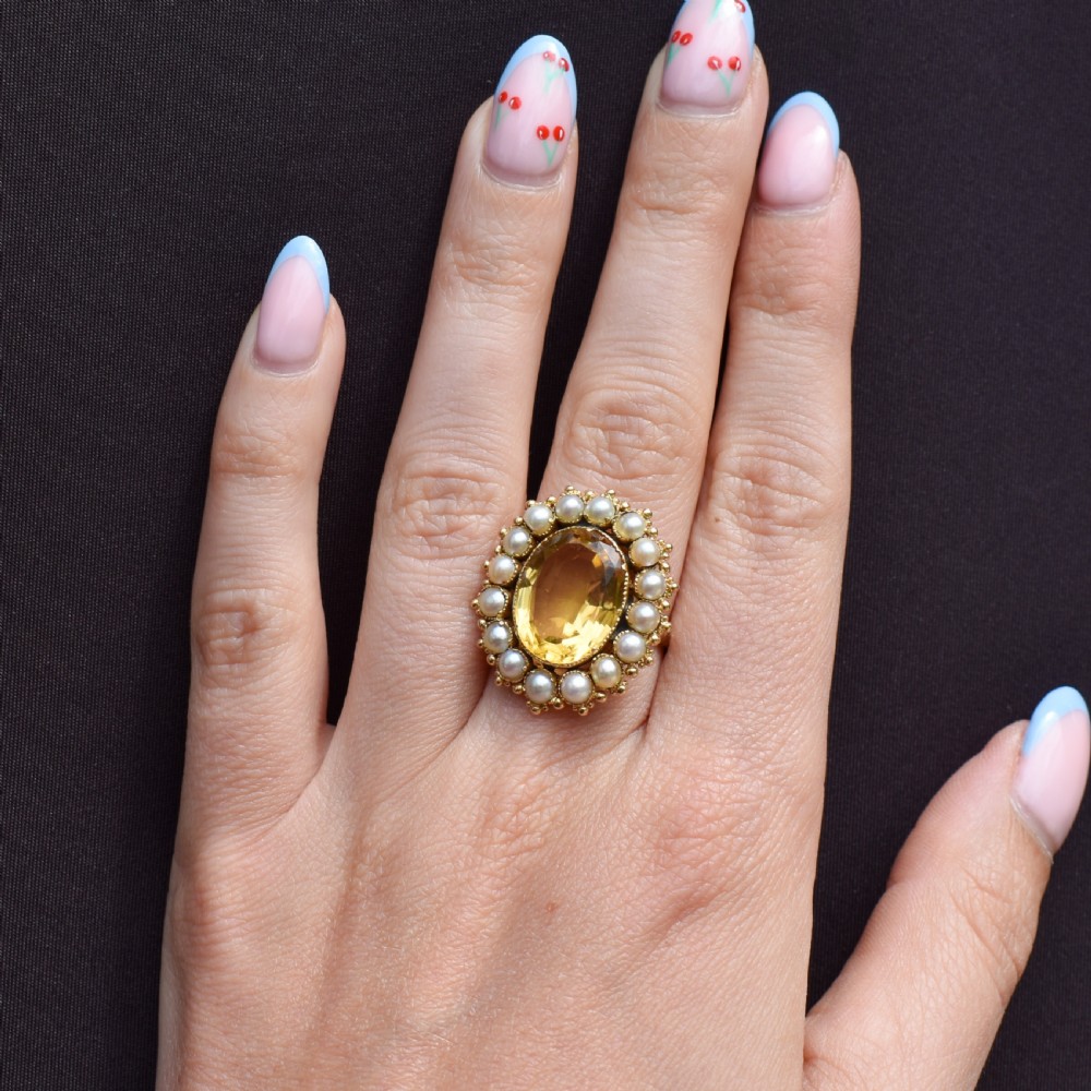An antique yellow gold ring featuring a central oval faceted yellow citrine stone surrounded by a halo of white seed pearls. View IV