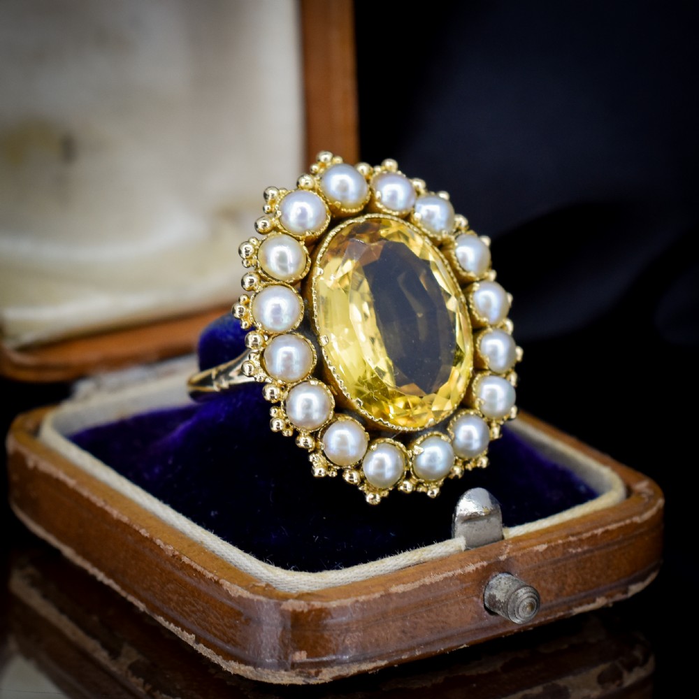 An antique yellow gold ring featuring a central oval faceted yellow citrine stone surrounded by a halo of white seed pearls. View VI