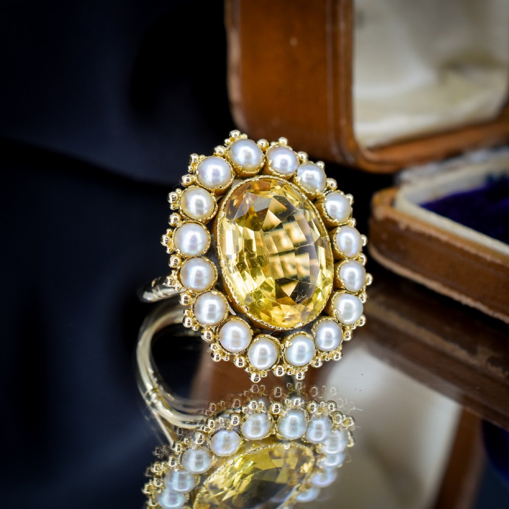 An antique yellow gold ring featuring a central oval faceted yellow citrine stone surrounded by a halo of white seed pearls. View VII