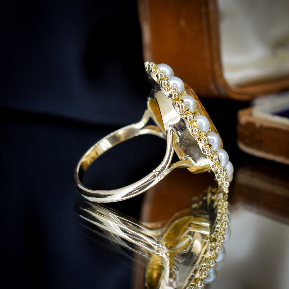 An antique yellow gold ring featuring a central oval faceted yellow citrine stone surrounded by a halo of white seed pearls. View VIII