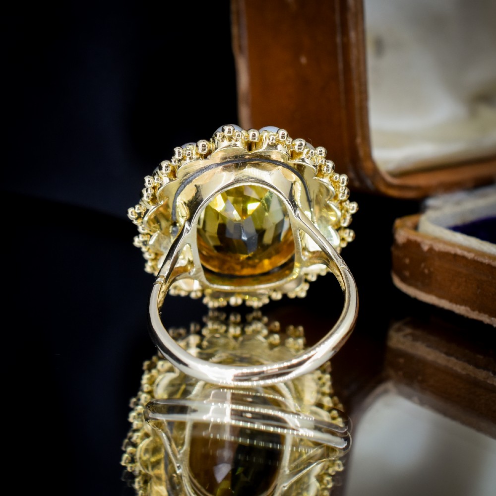 An antique yellow gold ring featuring a central oval faceted yellow citrine stone surrounded by a halo of white seed pearls. View IX