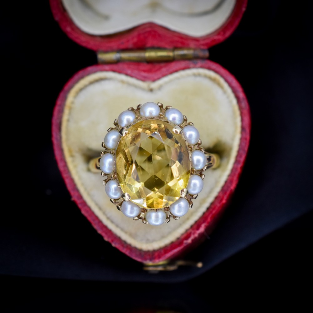 A vintage 9ct gold ring featuring a central oval faceted yellow citrine gemstone surrounded by a halo of small white pearls.