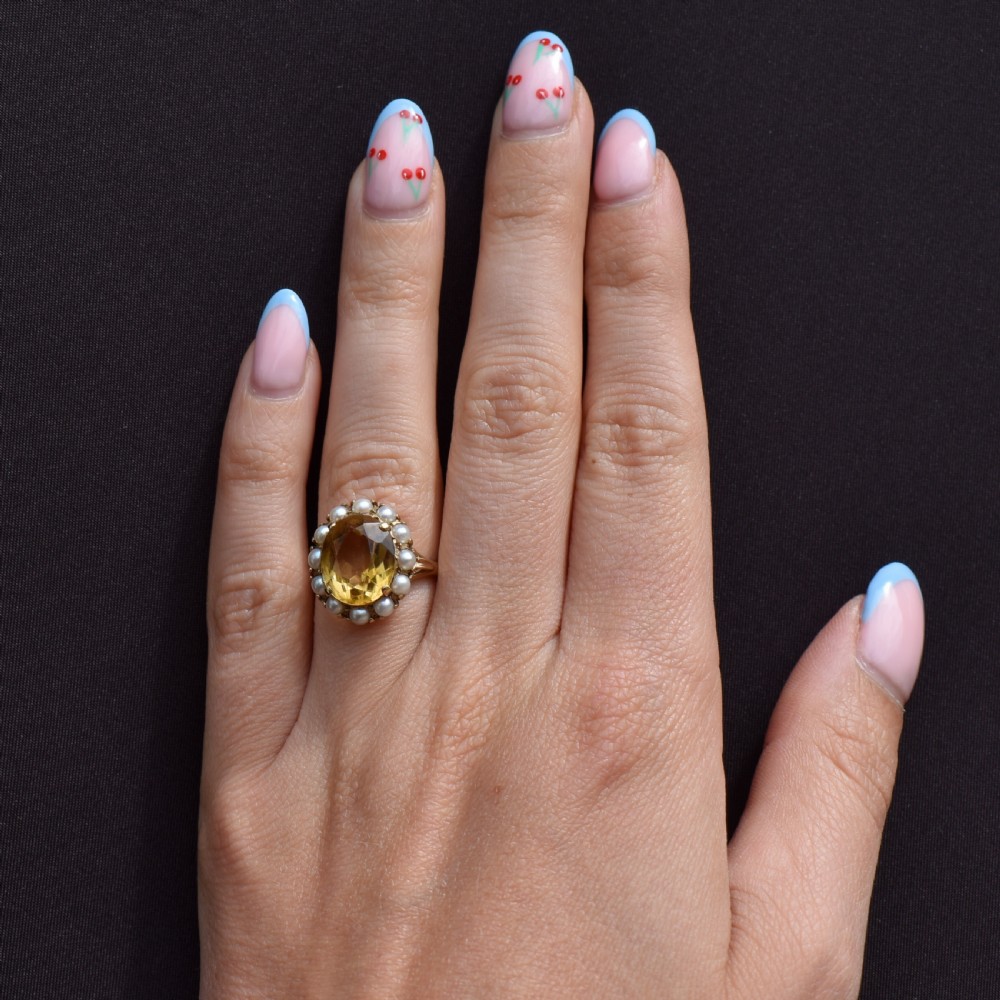 A vintage 9ct gold ring featuring a central oval faceted yellow citrine gemstone surrounded by a halo of small white pearls. View X