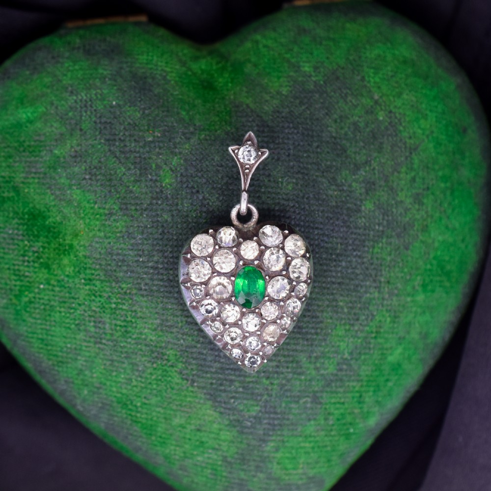 A heart-shaped sterling silver pendant set with clear paste stones surrounding a central green paste stone. View II
