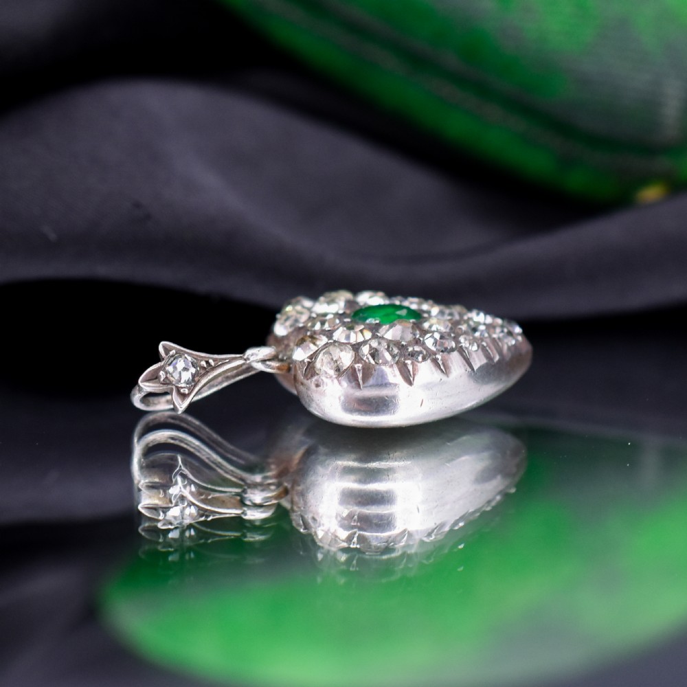 A heart-shaped sterling silver pendant set with clear paste stones surrounding a central green paste stone. View IV