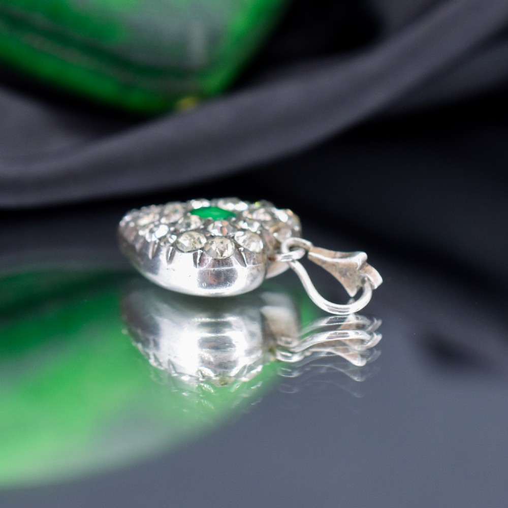 A heart-shaped sterling silver pendant set with clear paste stones surrounding a central green paste stone. View III