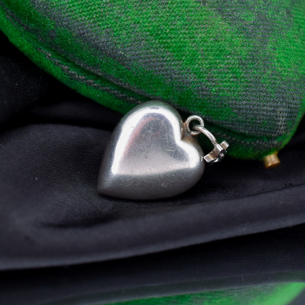 A heart-shaped sterling silver pendant set with clear paste stones surrounding a central green paste stone. View VII