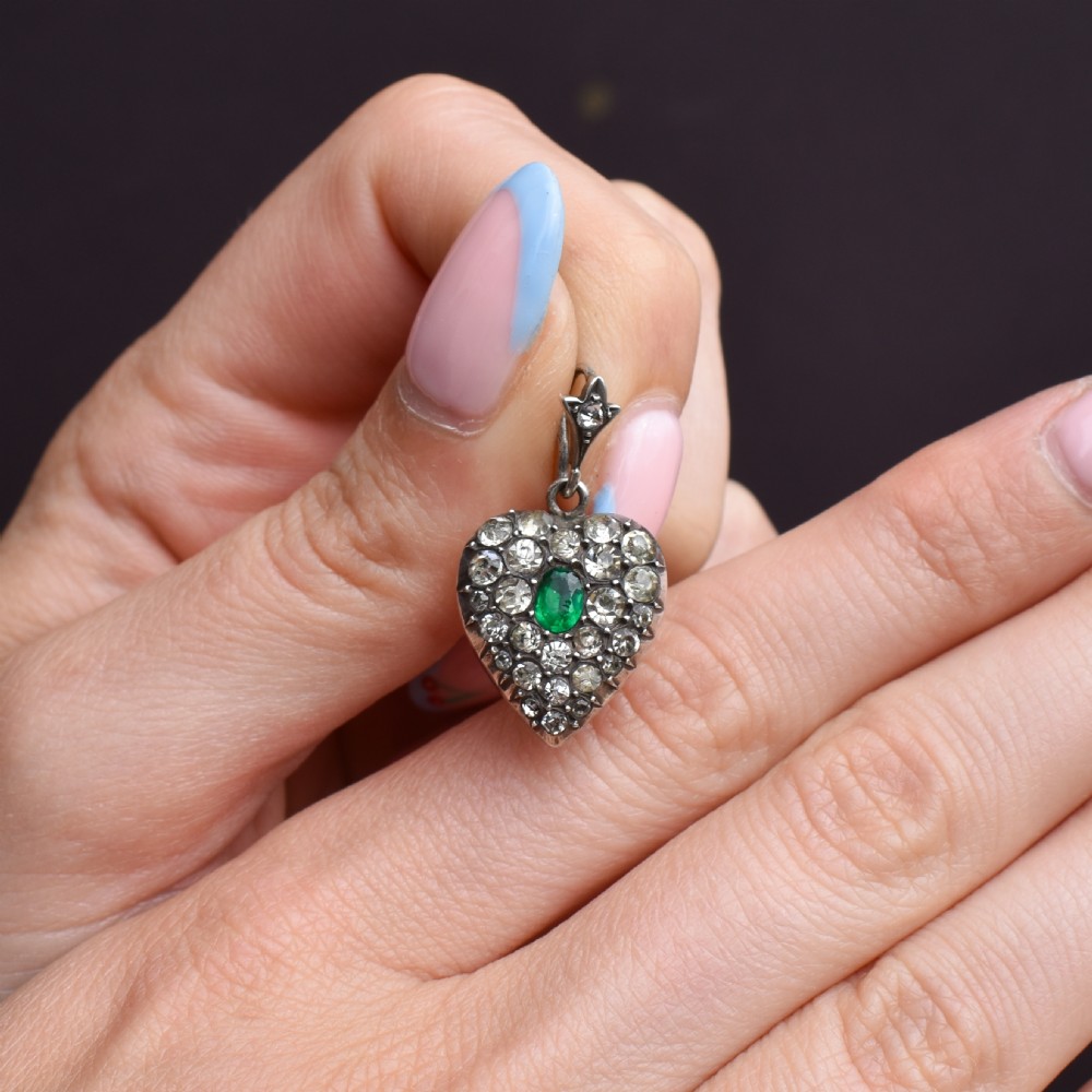 A heart-shaped sterling silver pendant set with clear paste stones surrounding a central green paste stone. View VIII