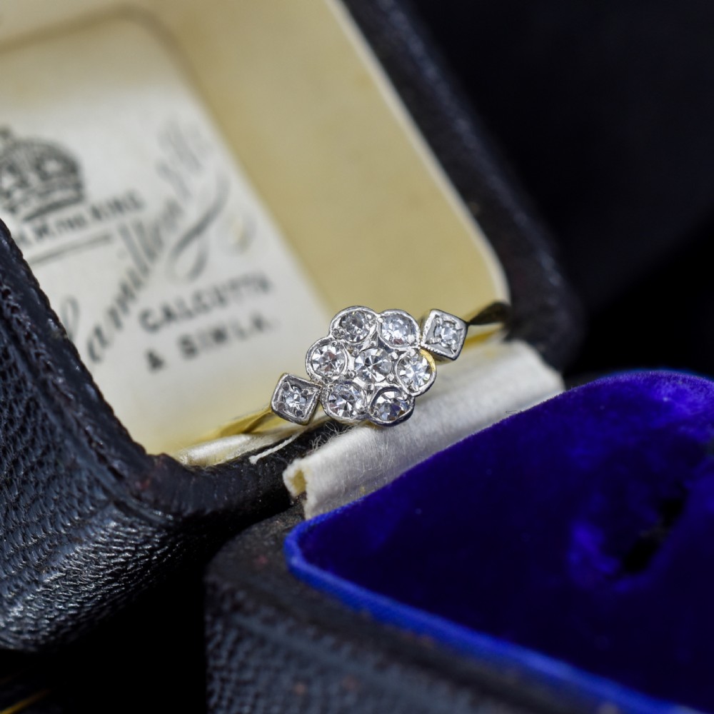 An Edwardian cluster ring crafted in yellow gold and platinum, featuring a central round diamond surrounded by a halo of diamonds with diamond-set shoulders.
