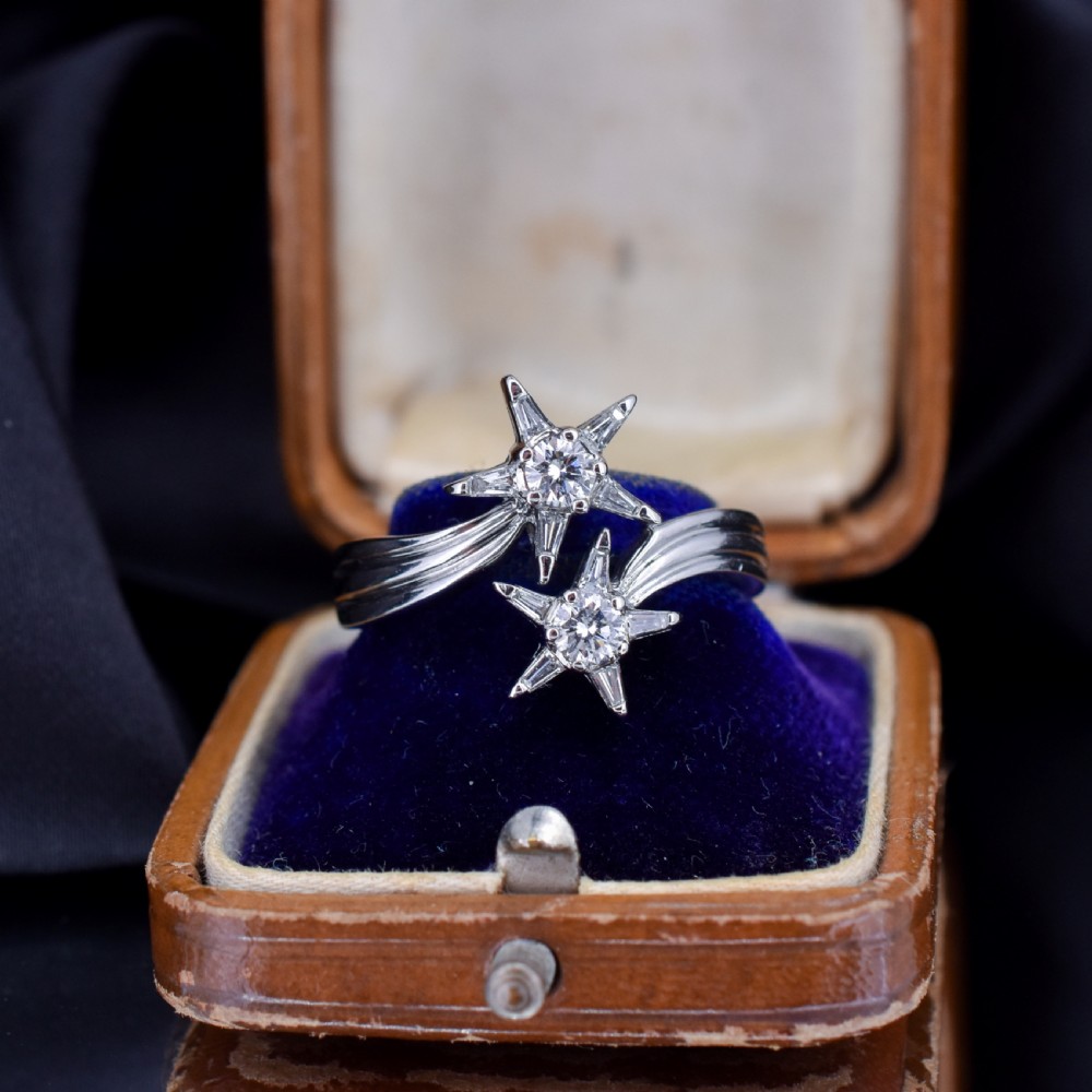 An 18ct white gold bypass ring featuring two star motifs set with brilliant-cut and baguette diamonds.