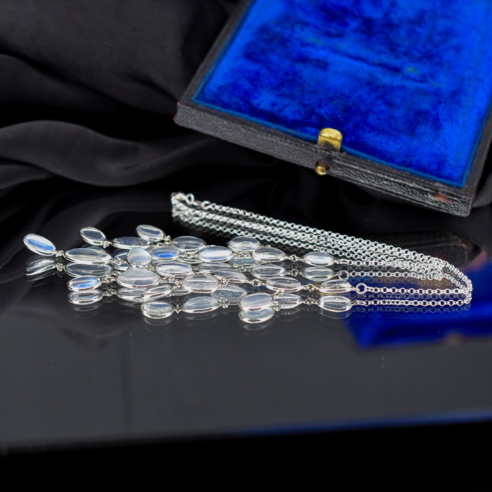 An antique silver festoon necklace featuring tiered oval cabochon moonstone drops suspended from a central chain. View VII