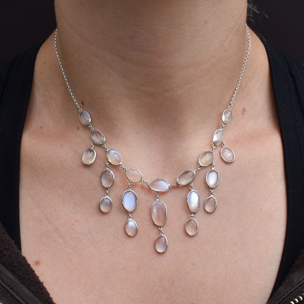 An antique silver festoon necklace featuring tiered oval cabochon moonstone drops suspended from a central chain. View IX