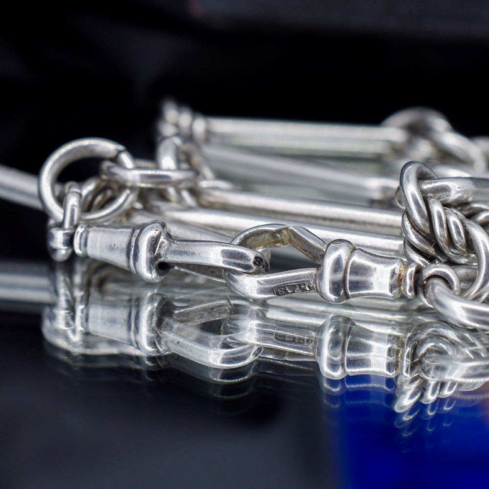 An antique sterling silver Albert watch chain featuring elongated trombone links interleaved with twisted love knots, complete with a T-bar and swivel clip. View VII