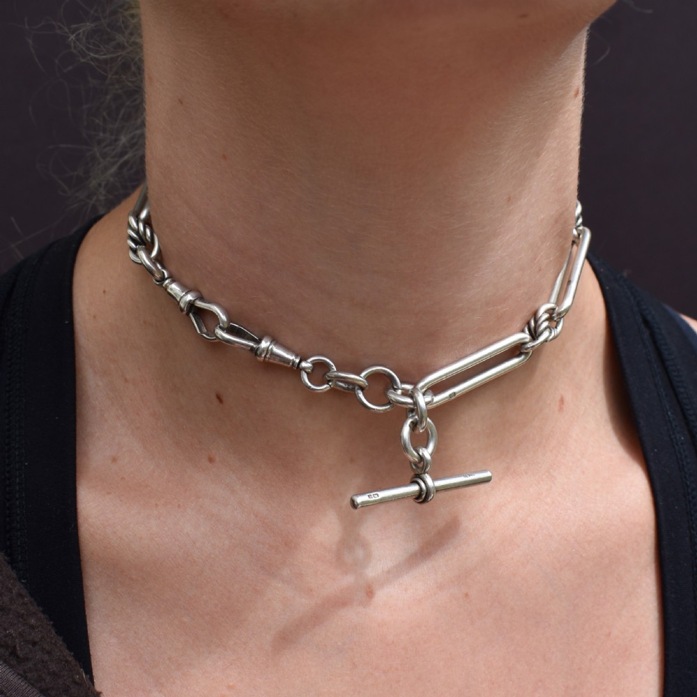 An antique sterling silver Albert watch chain featuring elongated trombone links interleaved with twisted love knots, complete with a T-bar and swivel clip. View IX