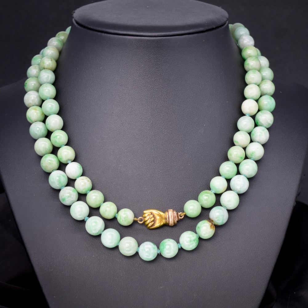 A double-strand necklace made of light green polished jade beads joined by a detailed gold hand-shaped figa clasp.