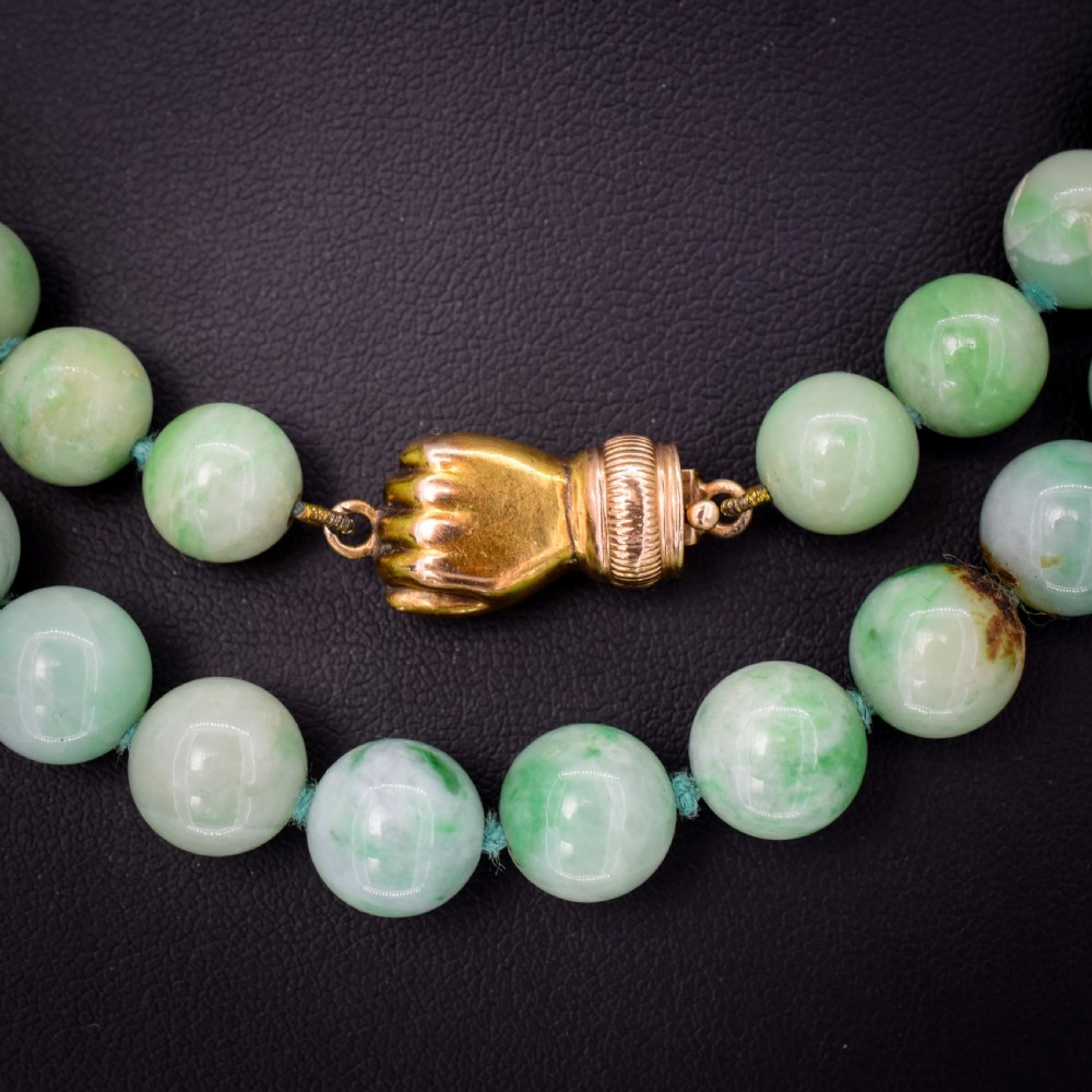 A double-strand necklace made of light green polished jade beads joined by a detailed gold hand-shaped figa clasp. View IV