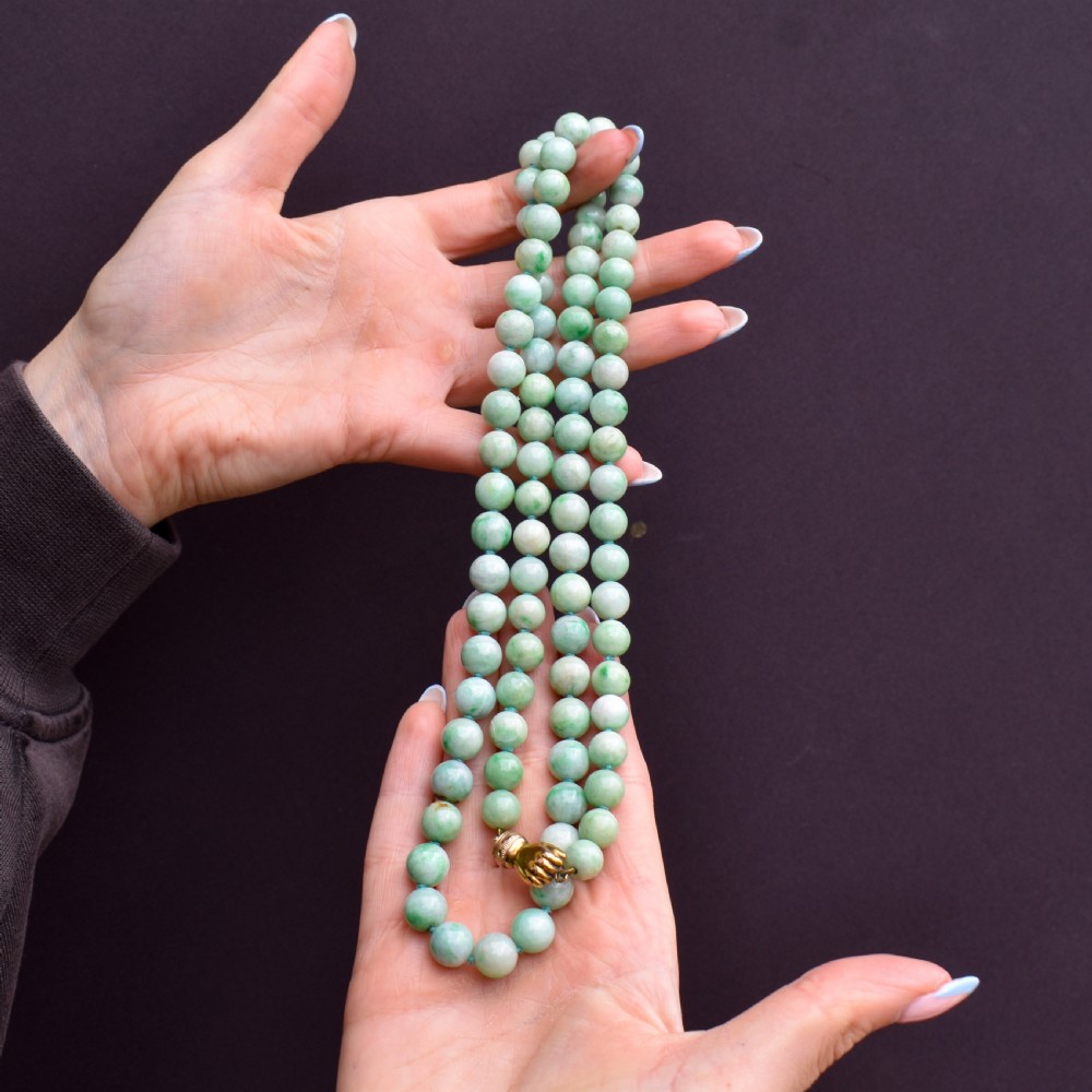 A double-strand necklace made of light green polished jade beads joined by a detailed gold hand-shaped figa clasp. View IX
