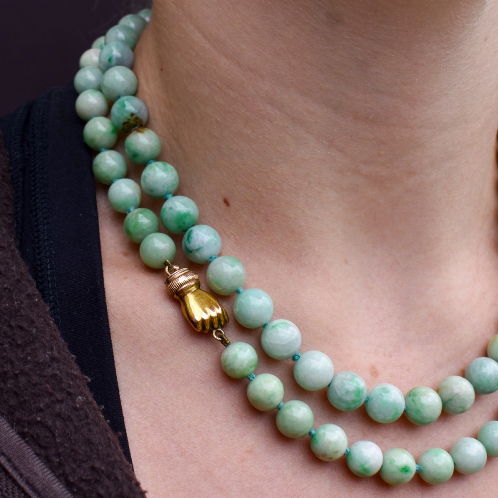 A double-strand necklace made of light green polished jade beads joined by a detailed gold hand-shaped figa clasp. View X