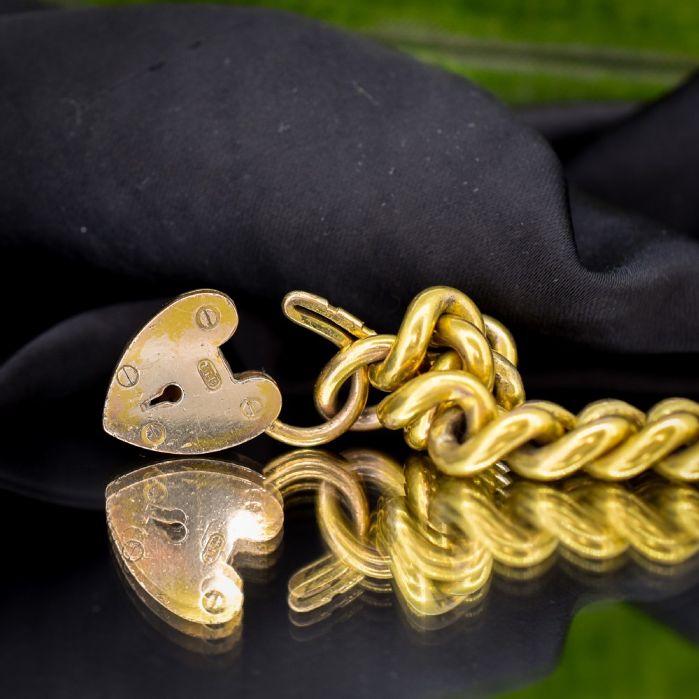 An antique rolled gold curb link bracelet featuring a heart-shaped padlock clasp and safety chain. View IV