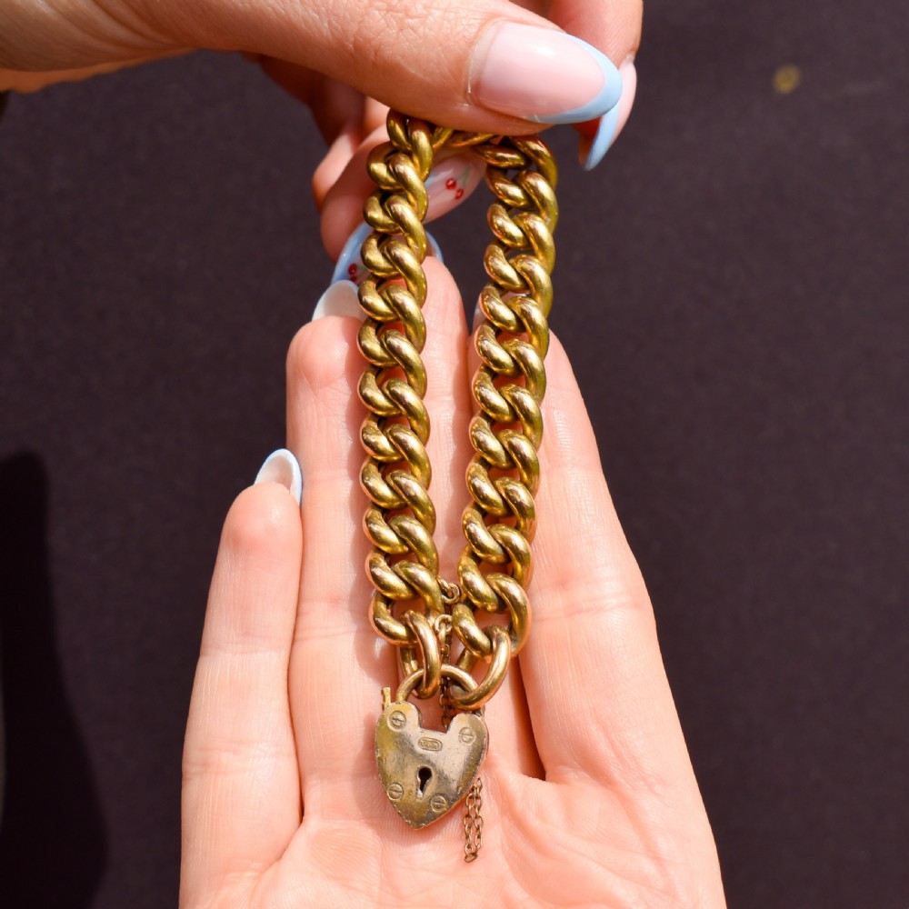 An antique rolled gold curb link bracelet featuring a heart-shaped padlock clasp and safety chain. View V