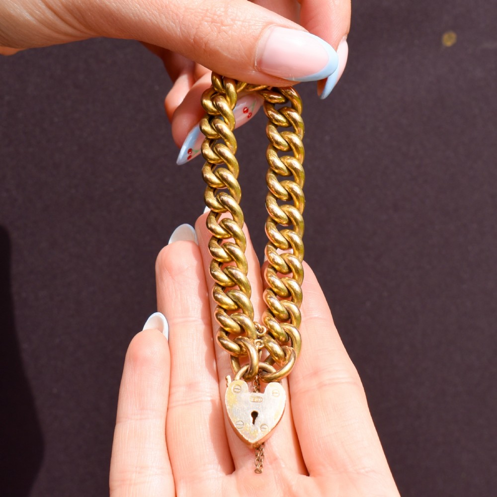 An antique rolled gold curb link bracelet featuring a heart-shaped padlock clasp and safety chain. View VI