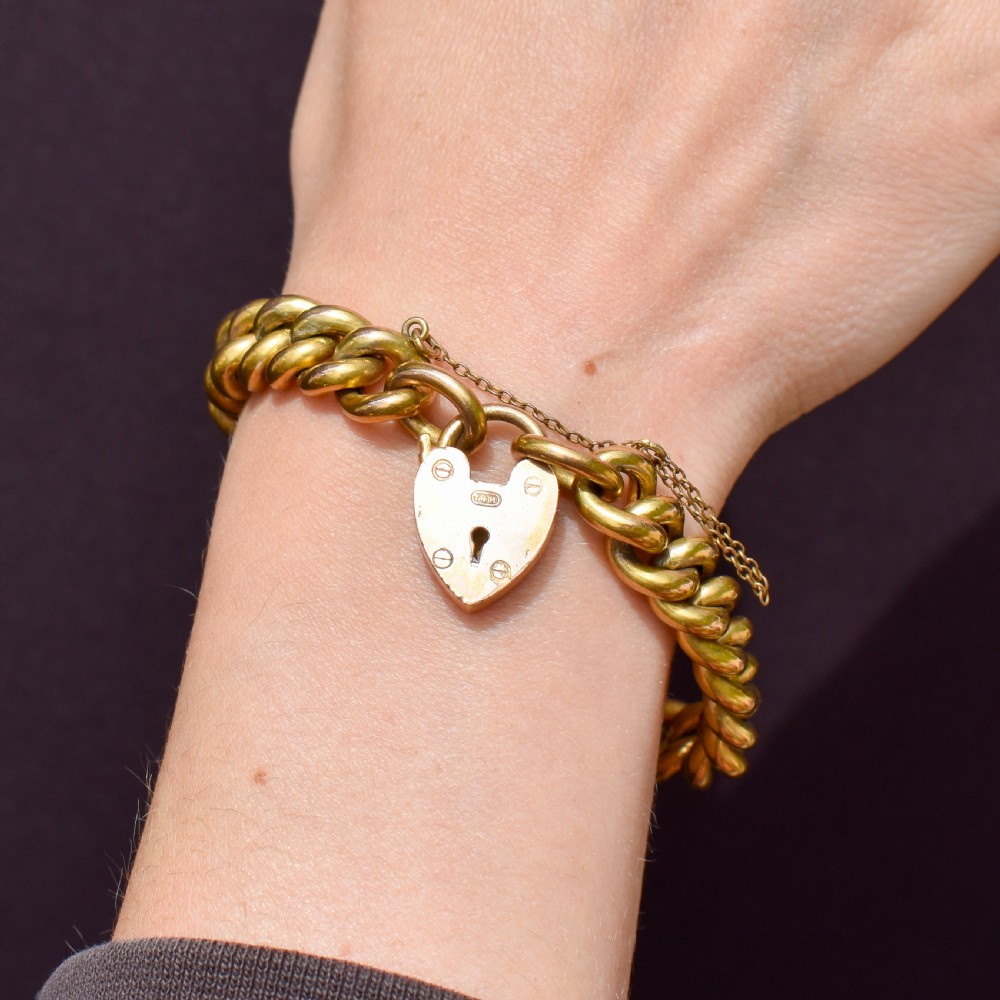 An antique rolled gold curb link bracelet featuring a heart-shaped padlock clasp and safety chain. View VII