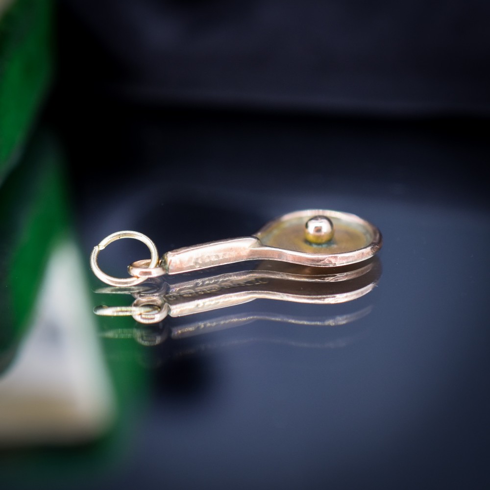 A small antique 9ct rose gold charm shaped like a tennis racket with a raised central tennis ball. View III